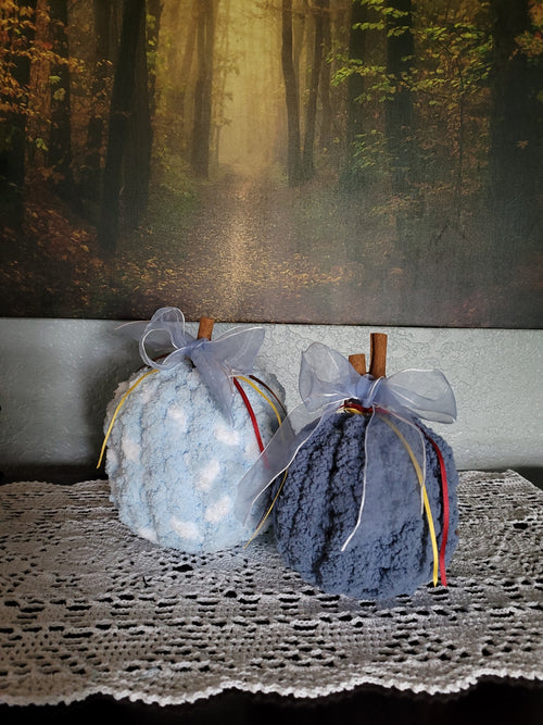 Hand‑knit blue chenille pumpkin pair with cinnamon‑stick stems and ribbon accents.
