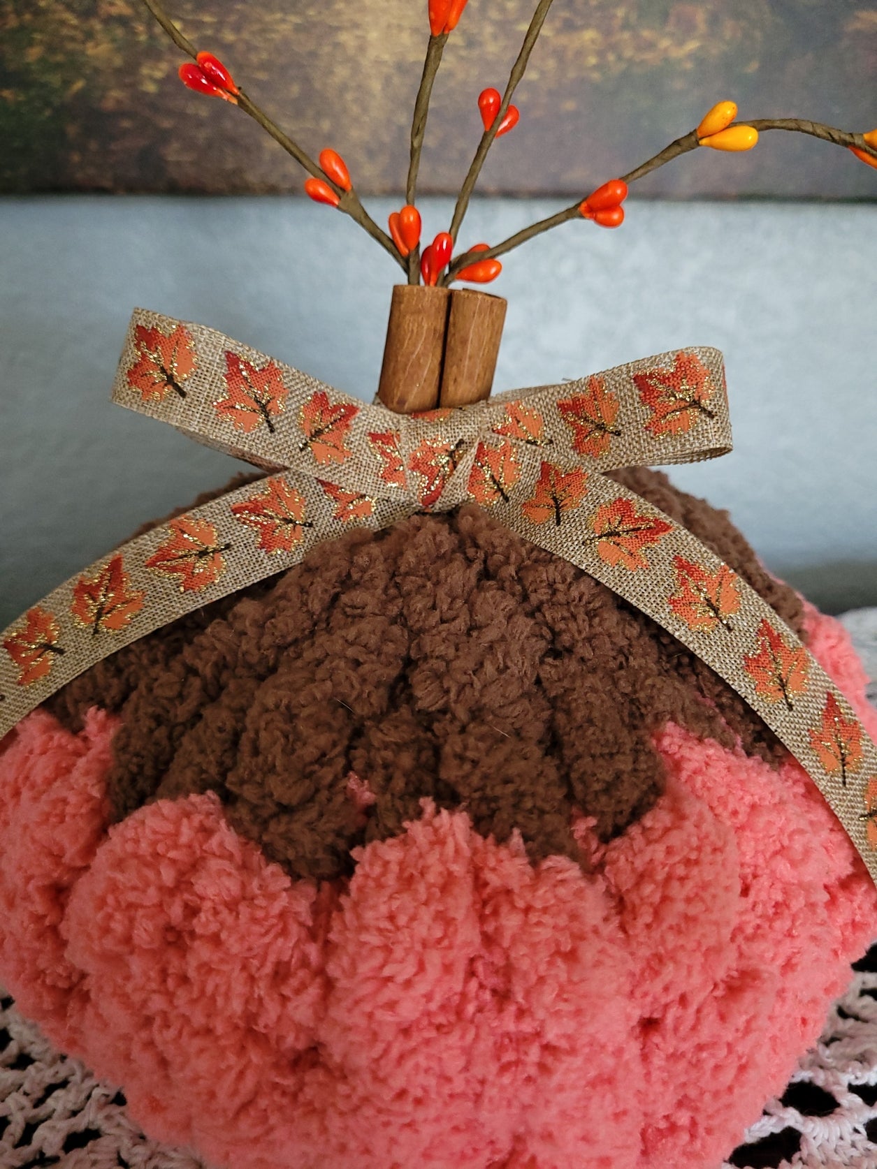 Close‑up of cinnamon‑stick stem, fall ribbon, and berry sprigs on handmade chenille pumpkin.