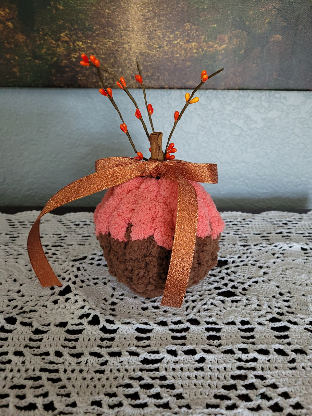Angled view of small chenille pumpkin with brown base, orange top, ribbon bow, and berry accents.